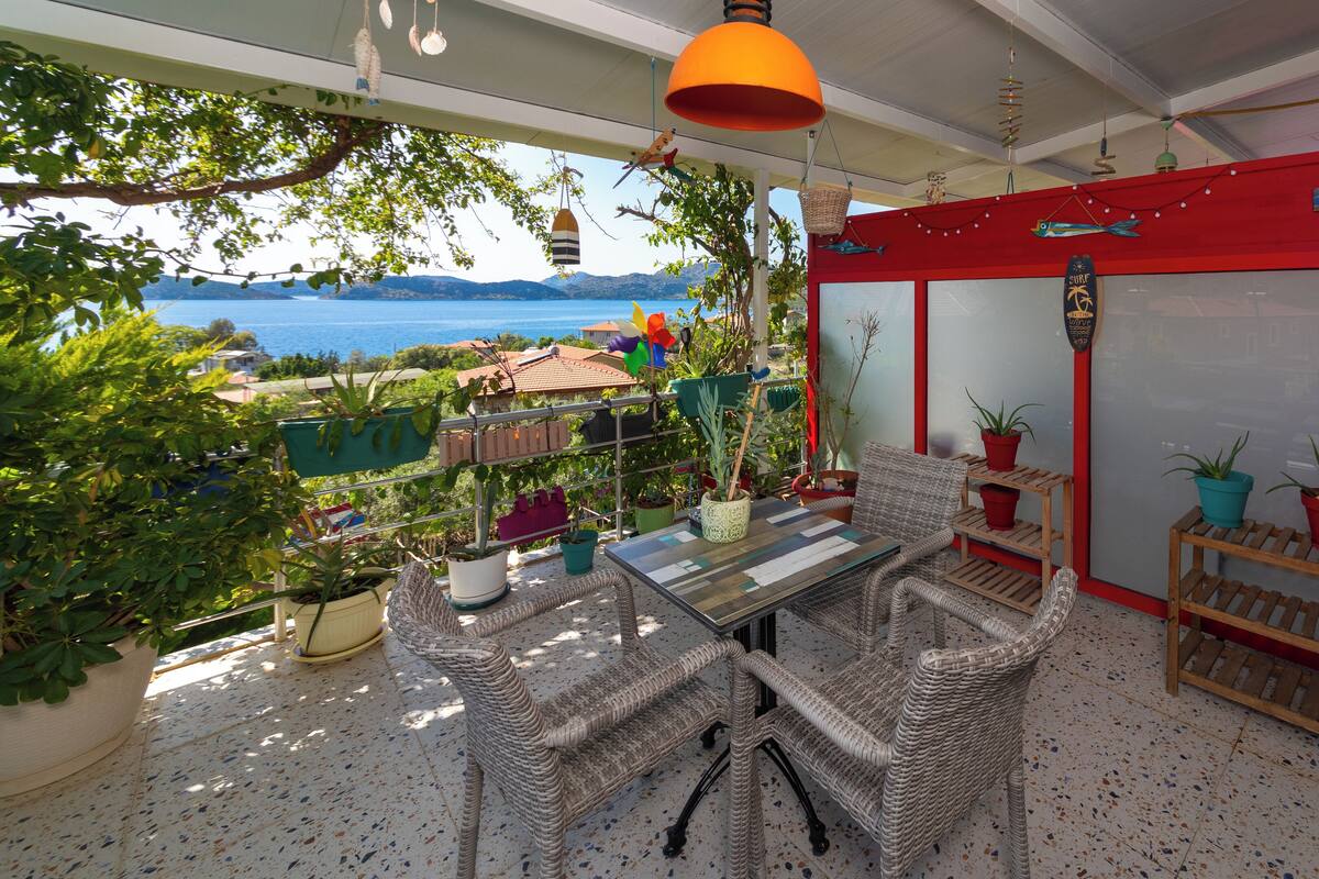 Een balkon met rieten meubilair, planten in potten en uitzicht op zee.