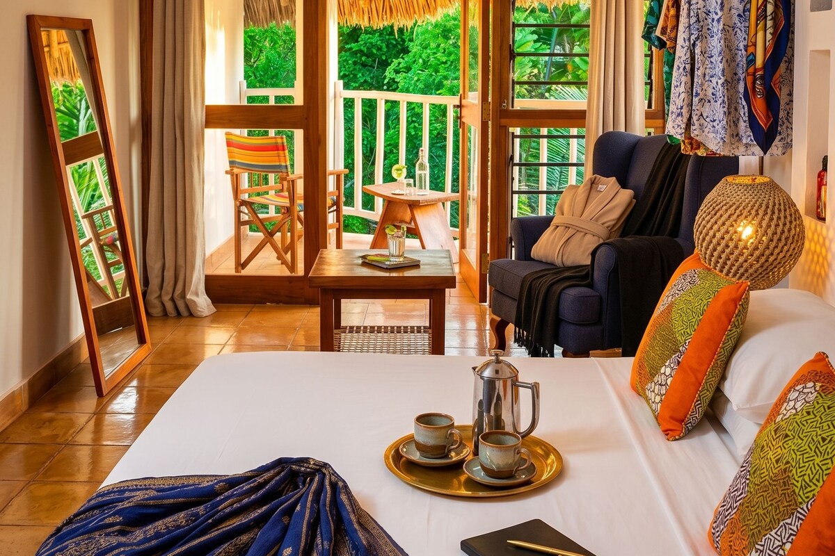 A room with a bed, a seating area with a table, and a view of greenery outside.
