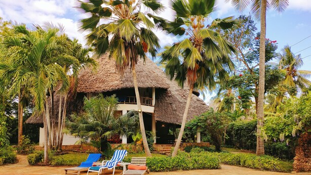 A pool area with lounge chairs, a thatched-roof structure, and palm trees. - Upani in Daini (Diani Beach)