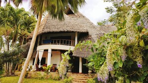 A thatched-roof house with a covered porch and a stone pathway leading to the entrance. - Upani in Daini (Diani Beach)