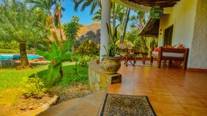 A covered patio with a pool, wooden furniture, and a decorative plant. - Upani in Daini (Diani Beach)
