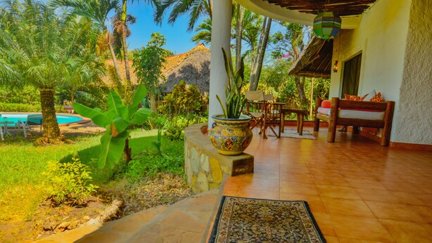 Un patio cubierto con piscina, mobiliario de madera y una planta decorativa.
