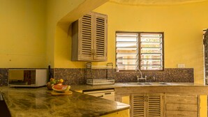 A kitchen with yellow walls, a microwave, a sink, and wooden cabinets. - Upani in Daini (Diani Beach)