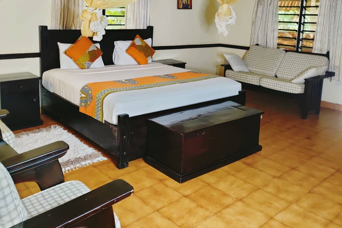 Quarto com cama, sofá, mesa de cabeceira e piso de madeira.