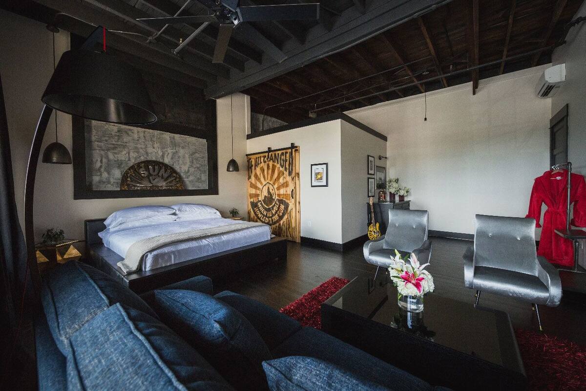 A modern bedroom with a bed, a sofa, and a chair. There is a painting on the wall and a poster.