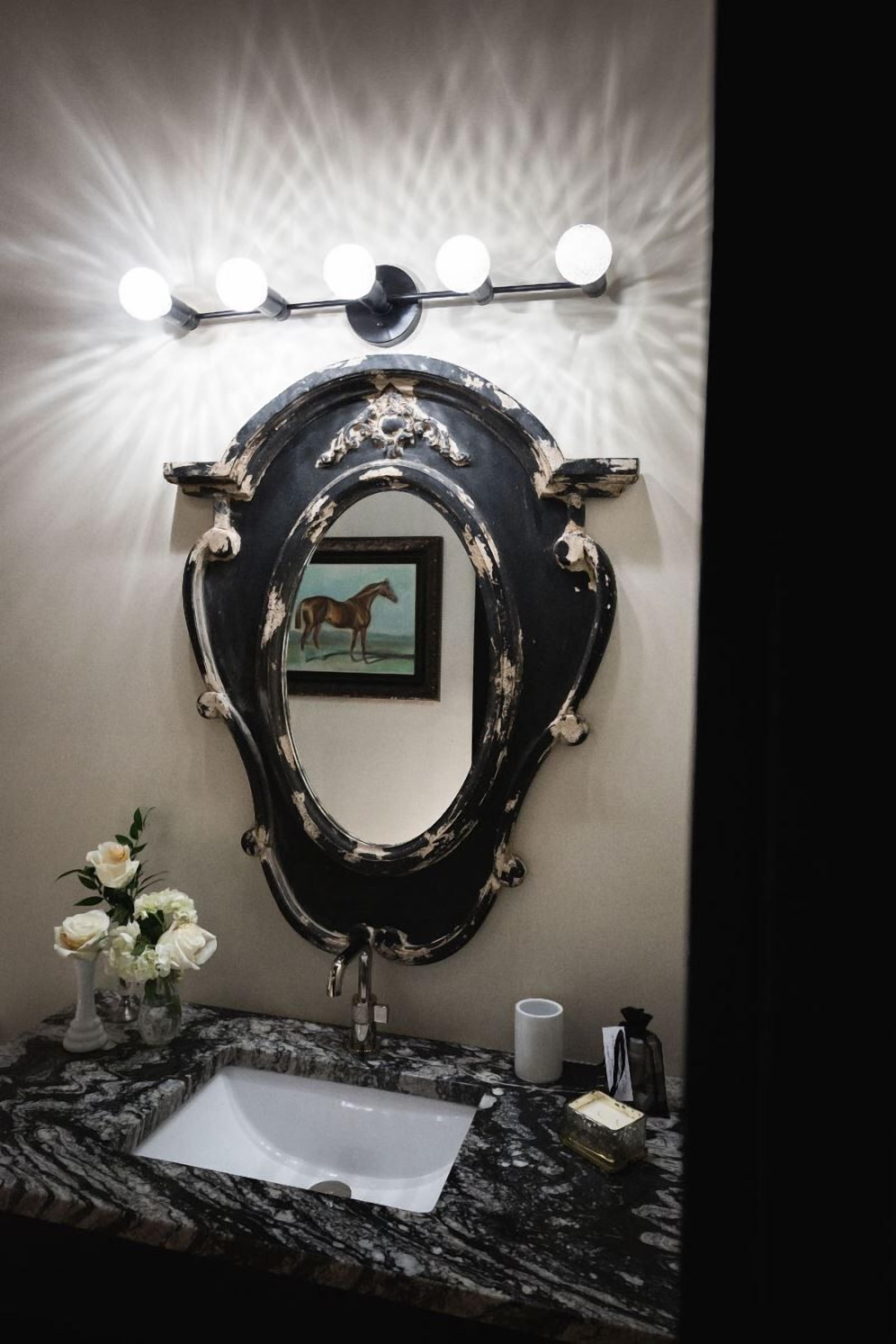 Een badkamer met een zwart sierlijk spiegel, een wastafel en een wastafelmeubel met een bloemenvaas.