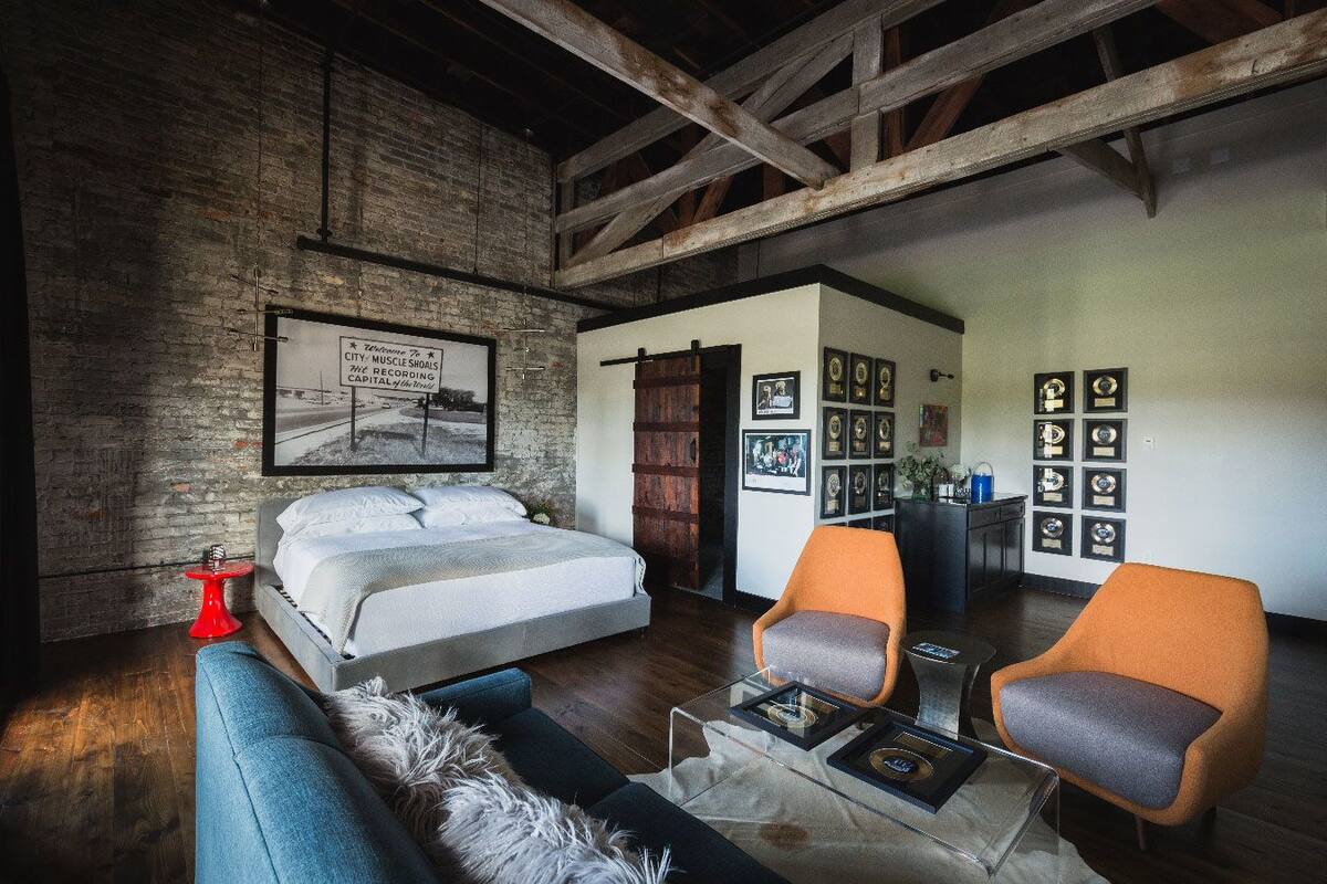 A bedroom with a bed, two chairs, a red table, and framed awards on the wall.
