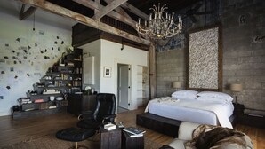 A spacious bedroom with a large bed, a chandelier, and a stone wall. - GunRunner Boutique Hotel (Florence)
