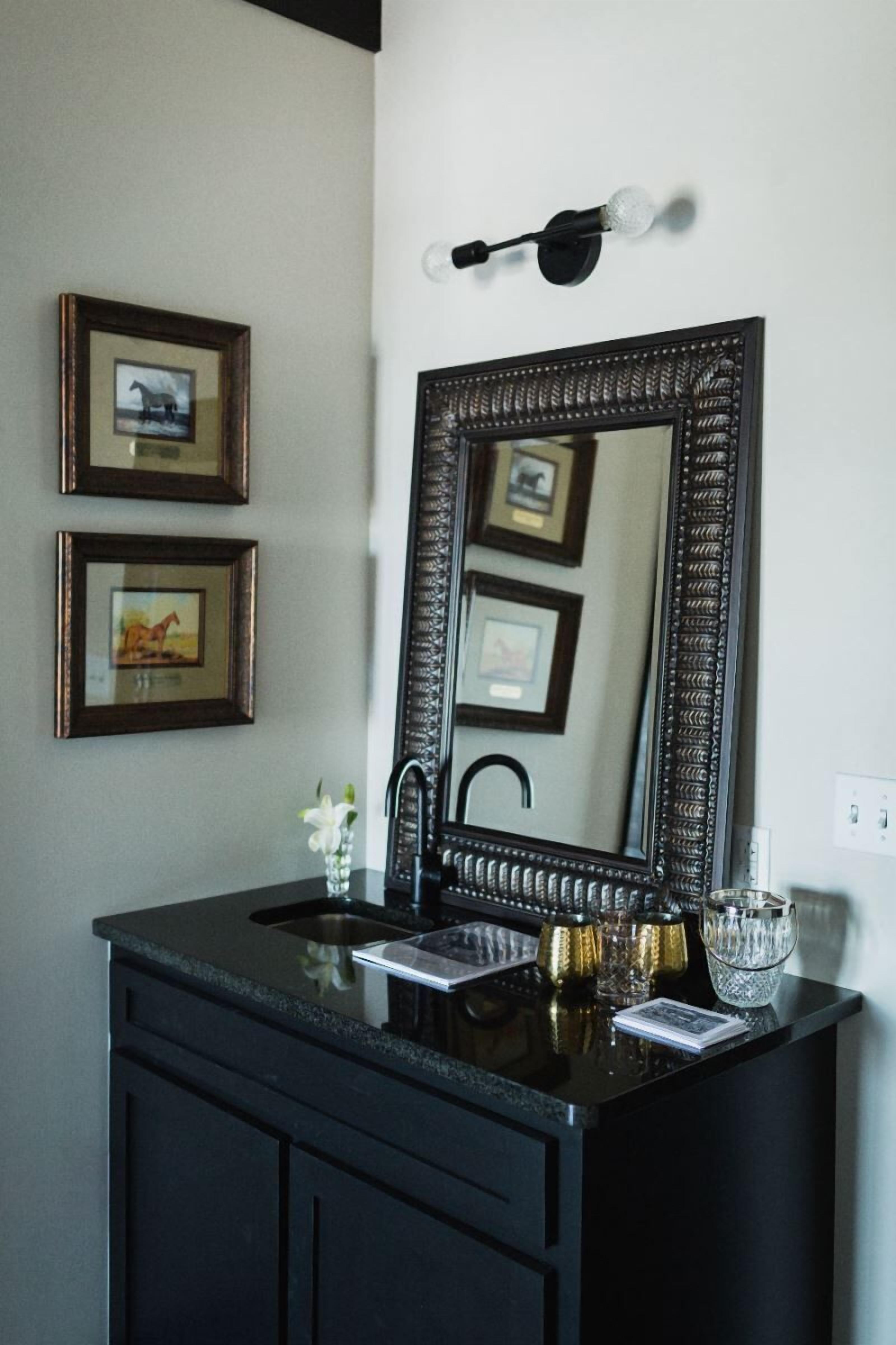 A bathroom vanity with a large mirror, a black countertop, and a sink. There are framed pictures on the wall above the vanity.