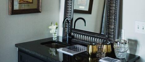 A bathroom vanity with a large mirror, a black countertop, and a sink. There are framed pictures on the wall above the vanity.
