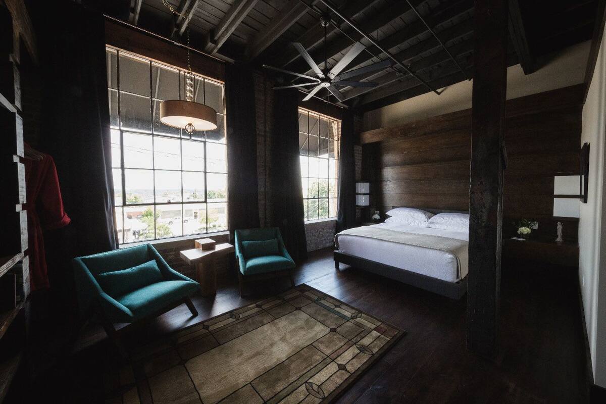 A bedroom with a large bed, two chairs, a small table, and a window with curtains.
