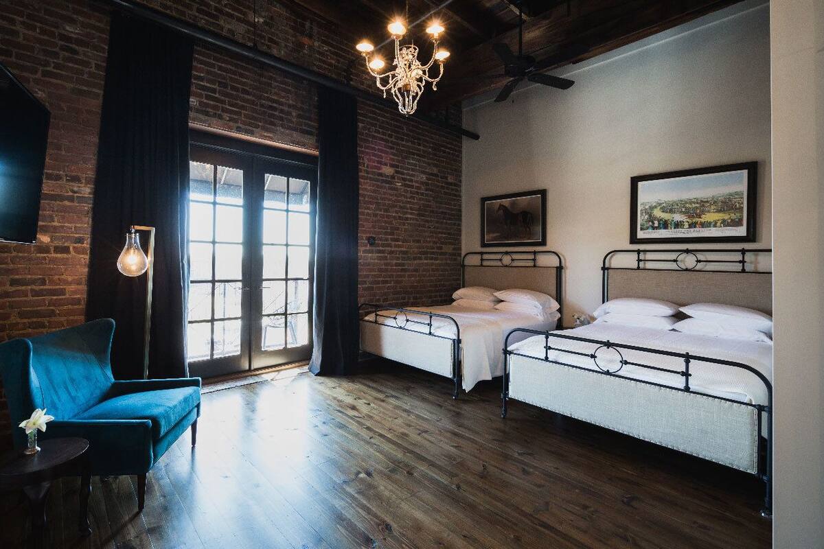 A room with two metal beds, a blue sofa, a chandelier, and a large window with curtains.