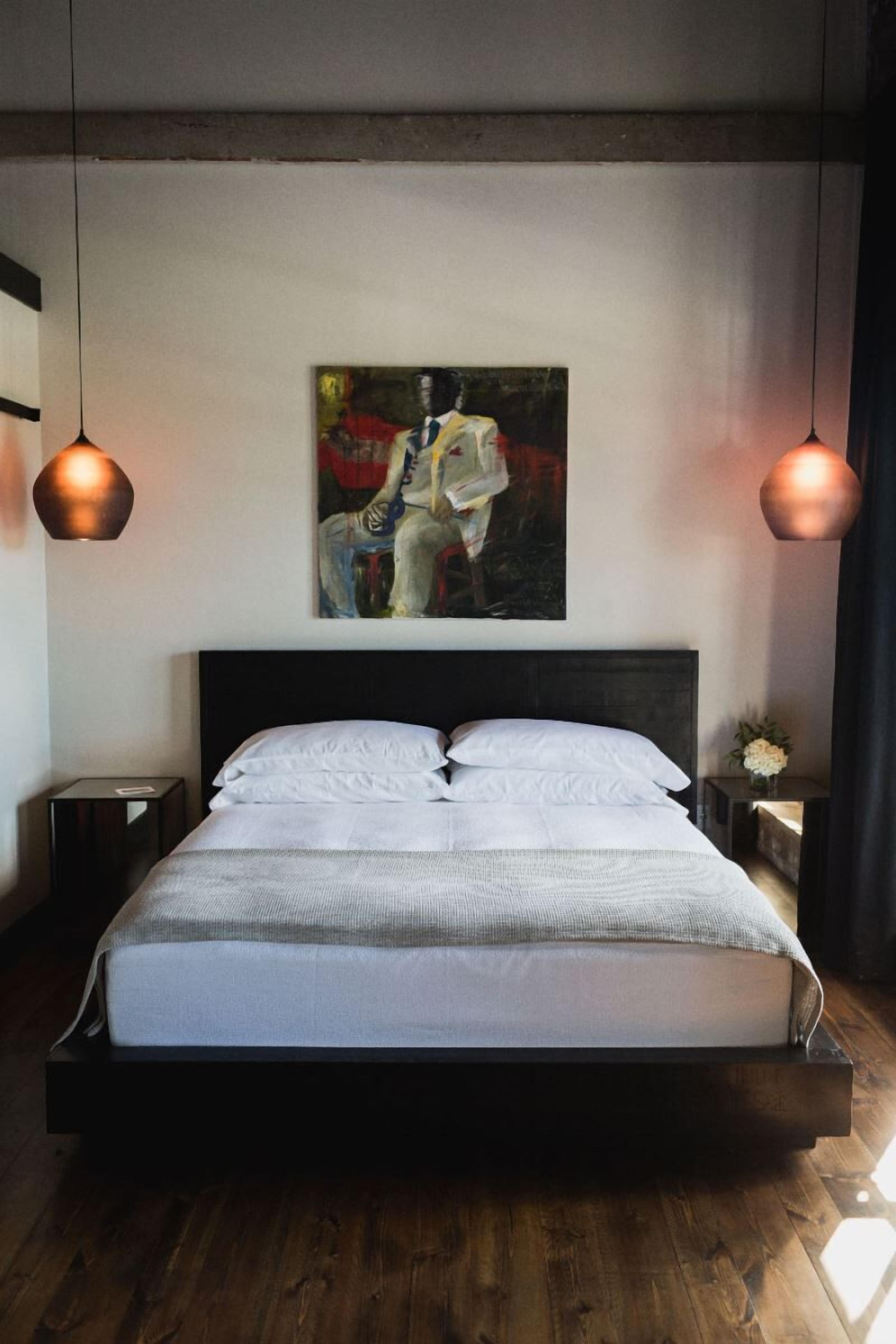 Een moderne slaapkamer met een groot bed, een schilderij aan de wand en twee hanglampen.