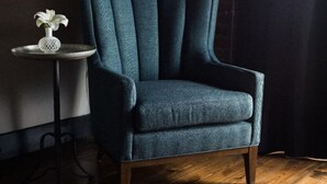 A teal armchair with wooden legs, a small round table with a white vase, and a hanging lamp. - GunRunner Boutique Hotel (Florence)