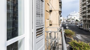 Un balcó amb vista a un carrer animat, un vaixell de creuer a la distància i edificis veïns.