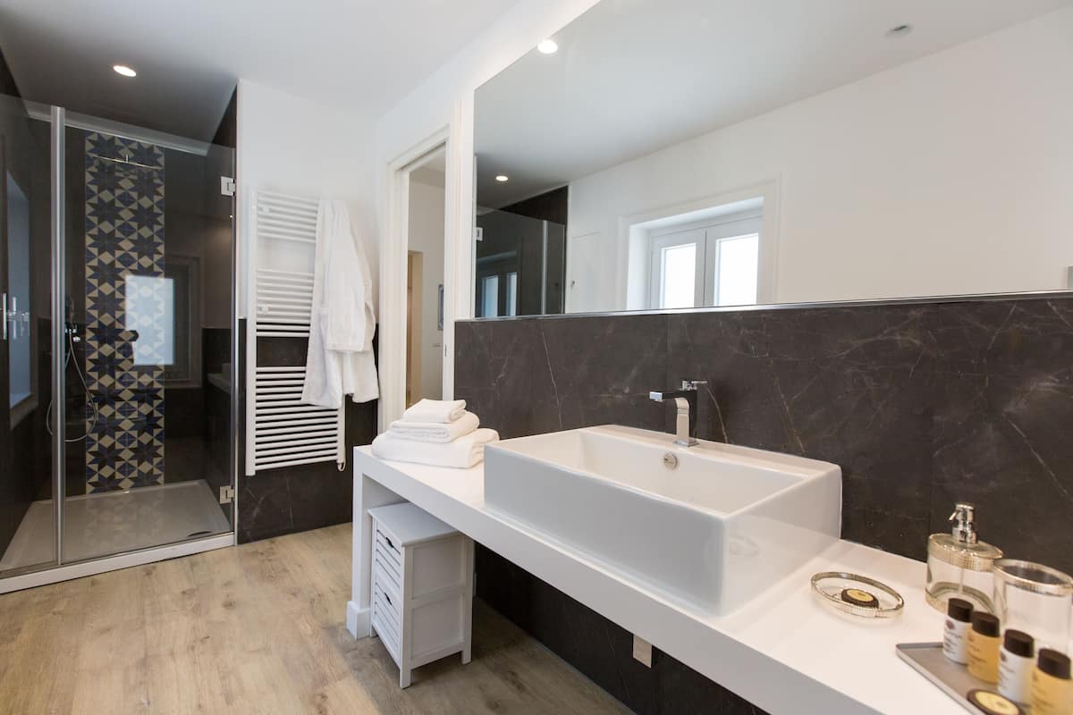 Ein modernes Badezimmer mit einem großen weißen Waschbecken, dunklen Marmorwänden und einer Duschkabine aus Glas.