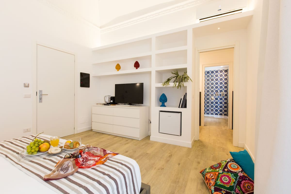 Ein modernes Schlafzimmer mit Bett, Fernseher, einer Minikühlschrank und einem Frühstücksangebot auf dem Bett.