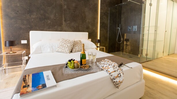 Habitació d'hotel moderna amb un llit gran, una dutxa de vidre i una taula de nit amb una ampolla de xampany i copes.