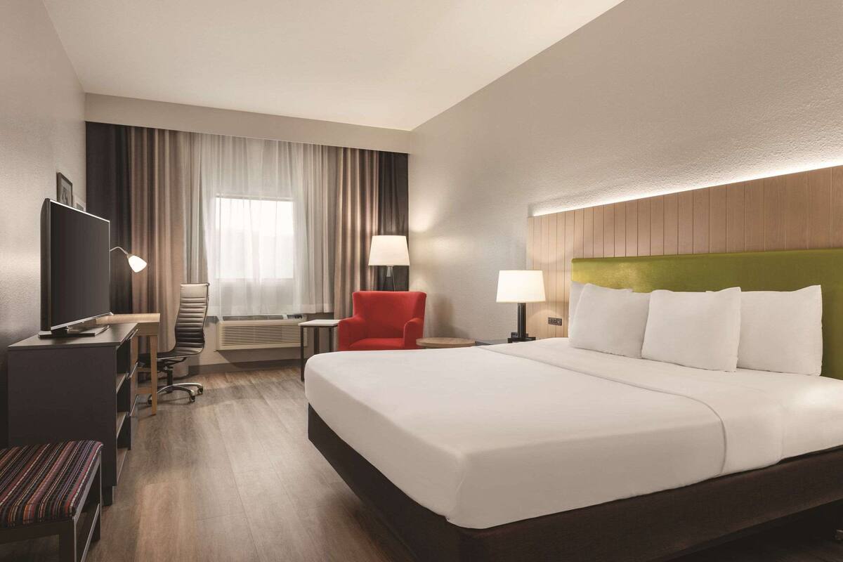 Una habitación de hotel con una cama grande, un escritorio con silla, televisión y ventana con cortinas.