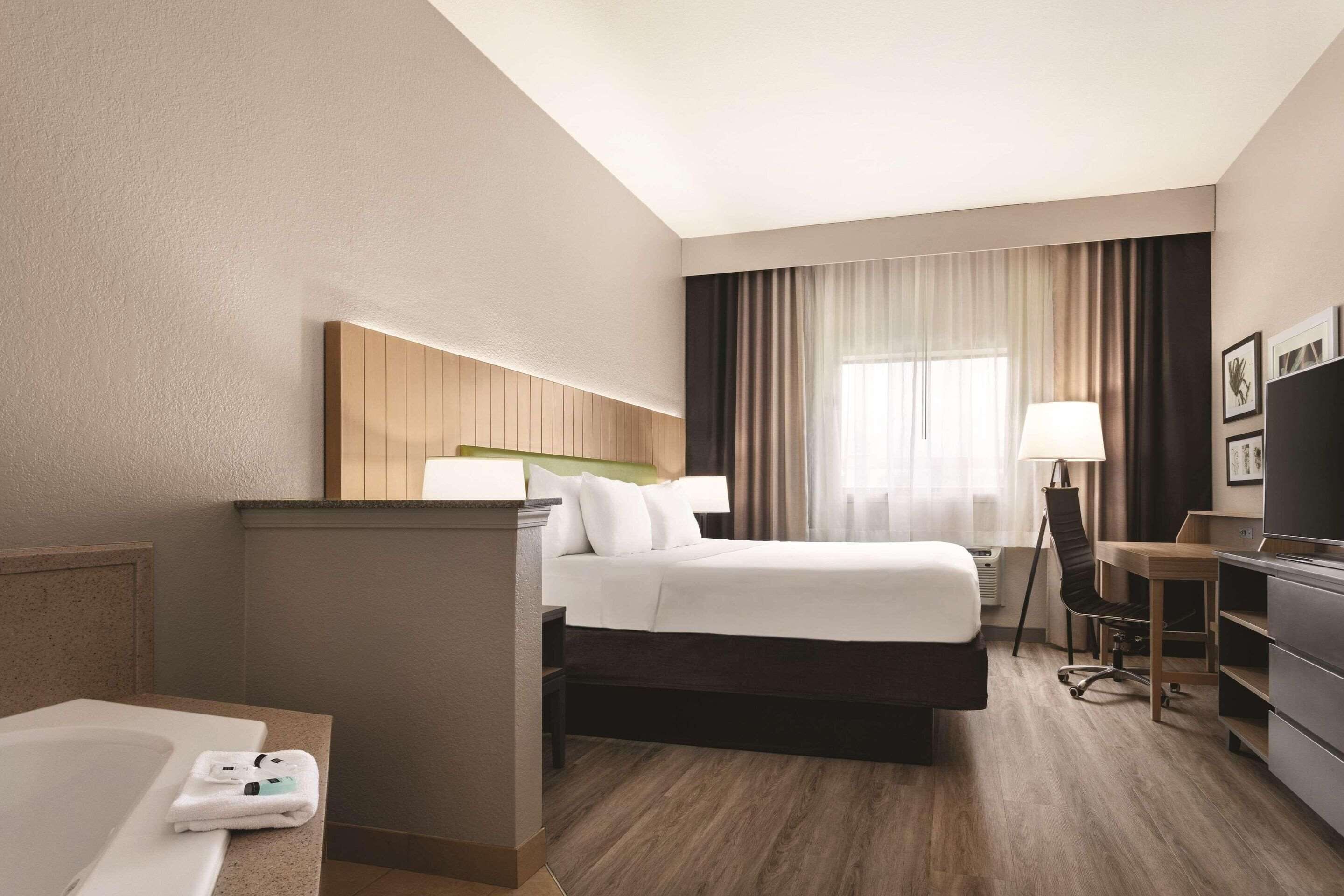 Una habitación de hotel con cama, escritorio, silla, televisión y zona de baño.