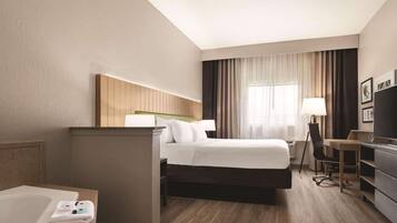 Una habitación de hotel con cama, escritorio, silla, televisión y zona de baño.