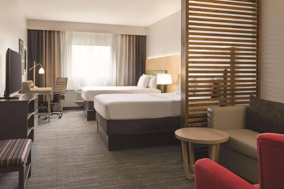 Una habitación de hotel con dos camas, un escritorio con silla, una mesita redonda y un sofá.