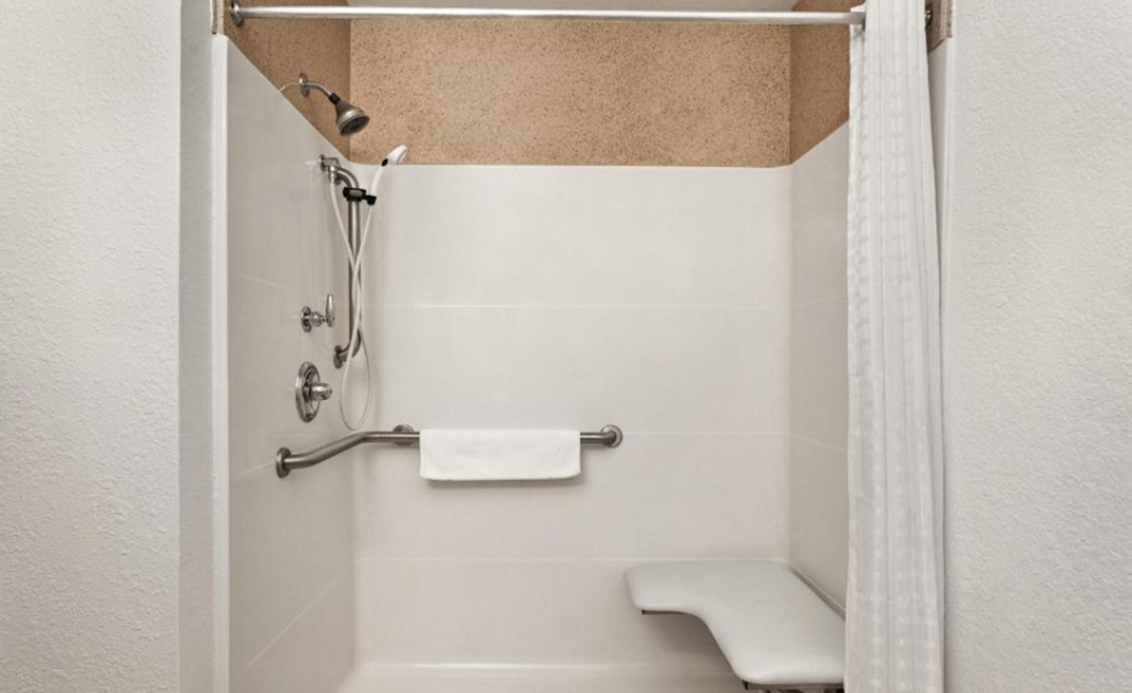 A small, enclosed shower area with a bench, grab bar, and towel rack.