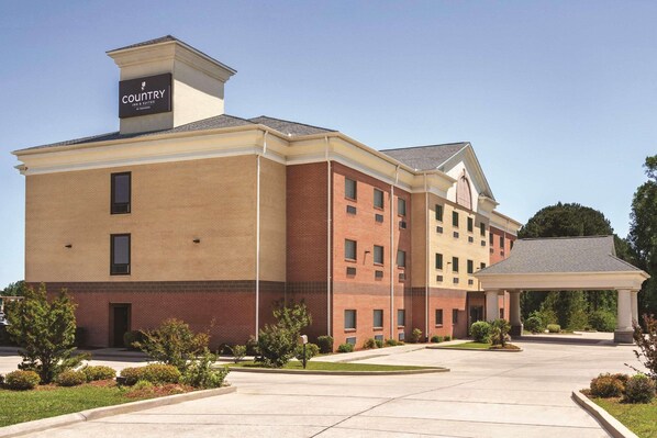 A multi-story hotel with a brick facade, a covered entrance, and a landscaped driveway.