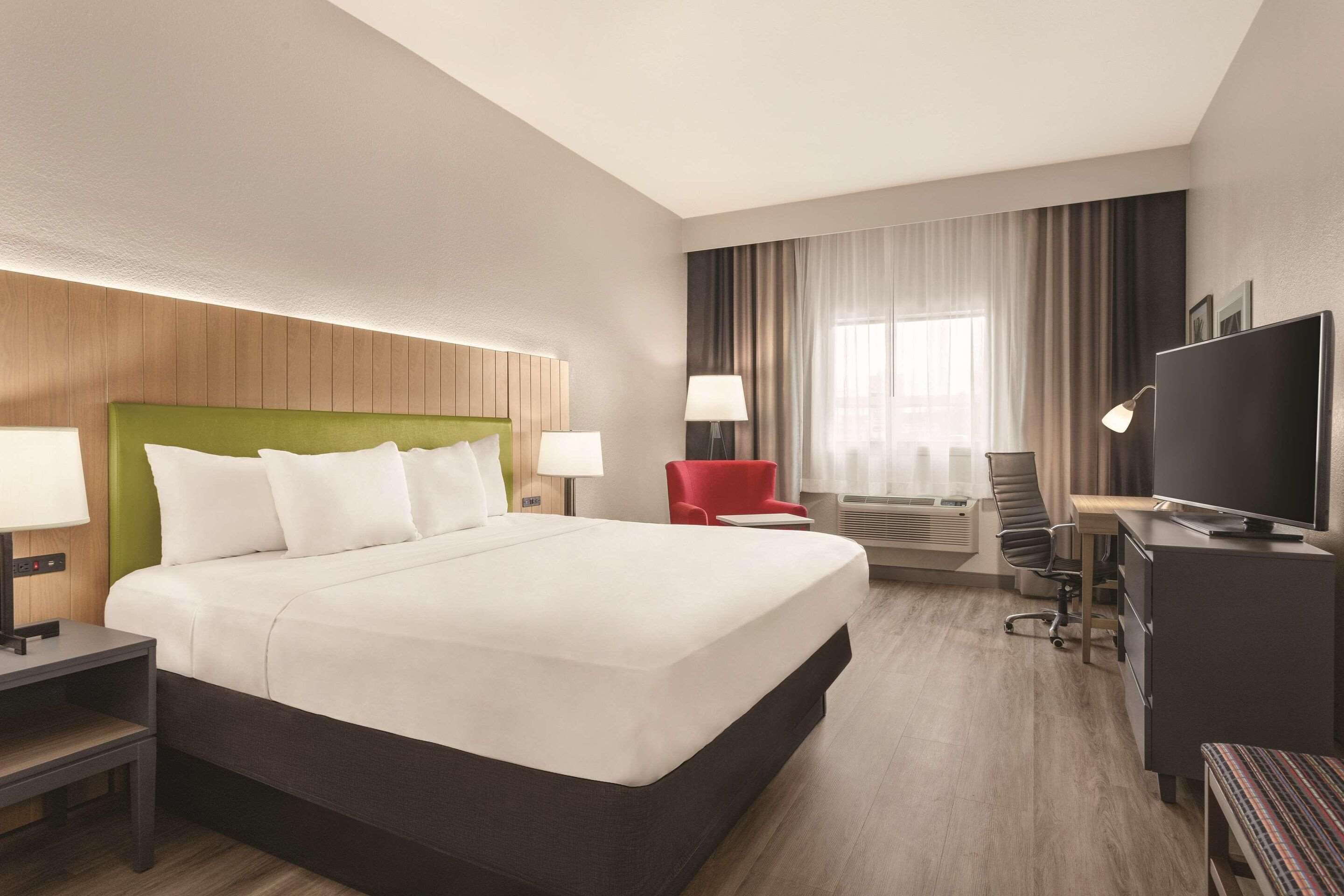 Habitación de hotel con una cama grande, un escritorio con televisión, una silla roja y una lámpara de escritorio.
