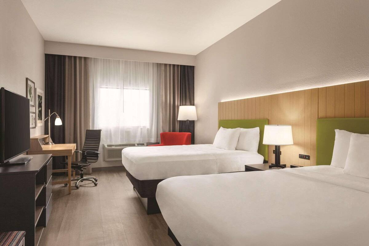 Habitación de hotel con dos camas, un escritorio con computadora, un televisor y una silla.