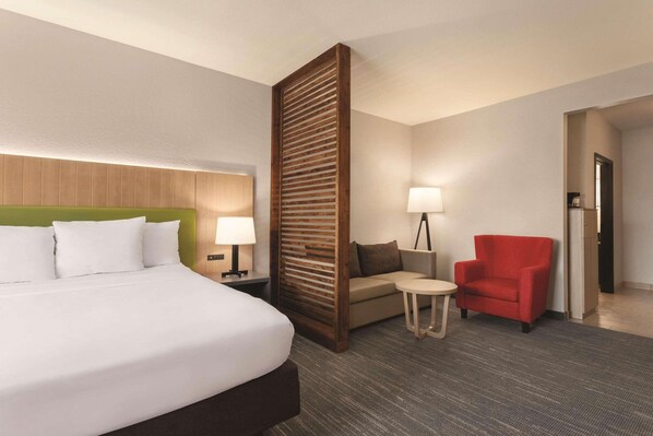 A hotel room with a large bed, a wooden headboard, a sofa, a red armchair, a small table, and a lamp.