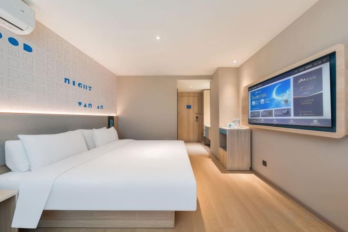 A modern hotel room with a large bed, a flat-screen TV, and a wall-mounted control panel.
