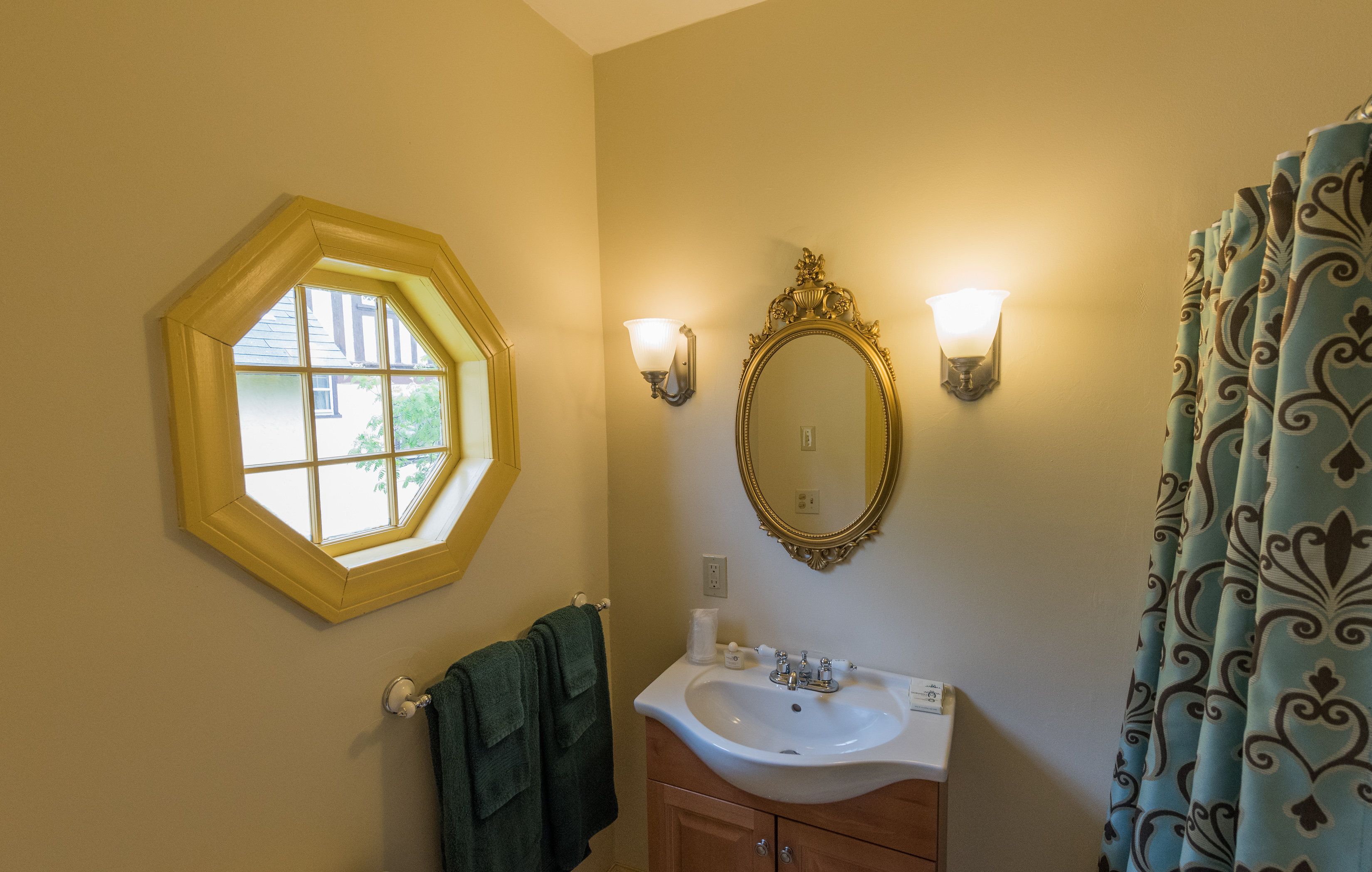 A bathroom with a hexagonal window, a wall-mounted mirror, a sink with a vanity, and a shower curtain.