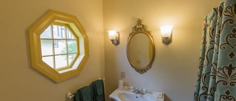 A bathroom with a hexagonal window, a wall-mounted mirror, a sink with a vanity, and a shower curtain.