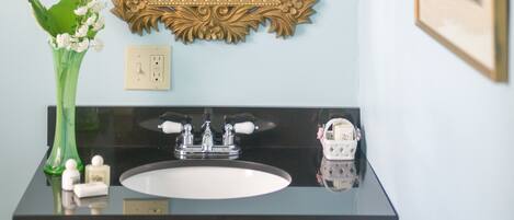 A bathroom with a gold-framed mirror, a black sink, and a green vase with flowers.