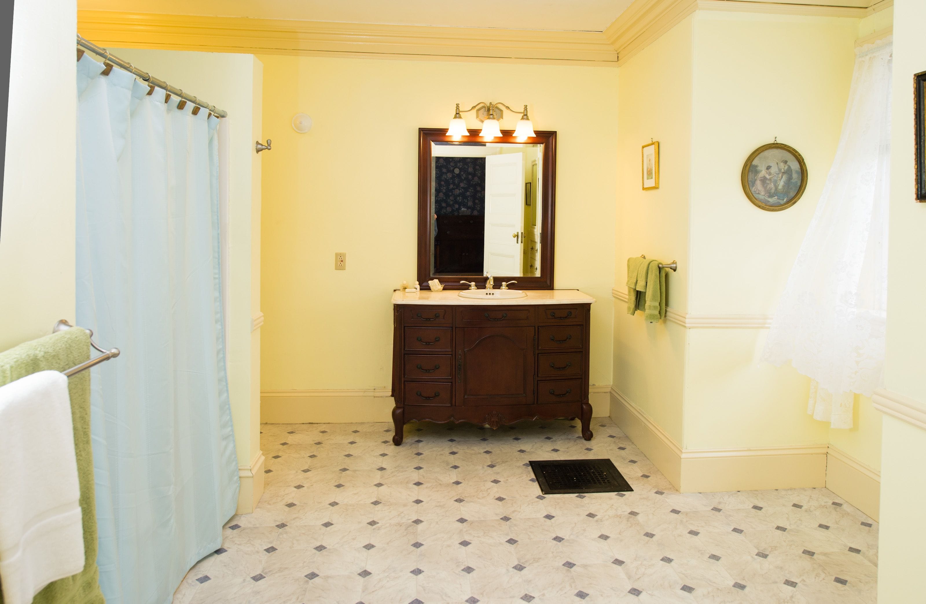 Un baño con tocador de madera, lavamanos, espejo con iluminación, cortina de ducha y baldosas de suelo con diseño.