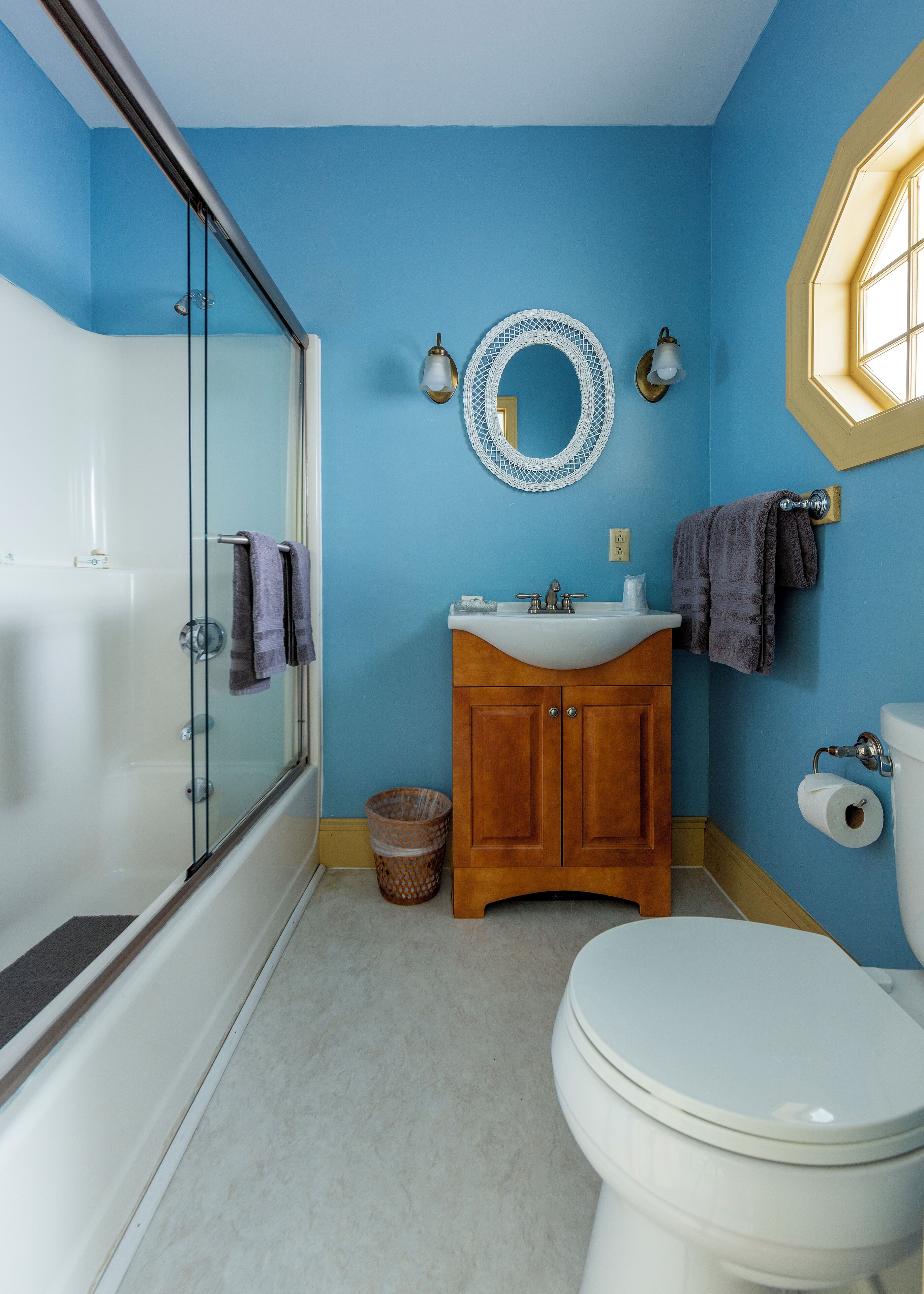 Un baño con cabina de ducha de vidrio, un tocador de madera con lavamanos, inodoro y un espejo redondo en la pared.