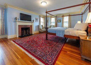 A four-poster bed with a red and blue patterned rug, a fireplace, and a television on the wall. - Thornhedge Inn & Stratford (Bar Harbor)
