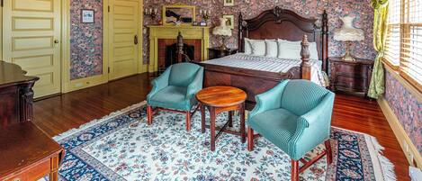 A room with a bed, two chairs, a table, a fireplace, and a chandelier.