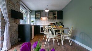 Uma cozinha com parede de pedra, uma TV de tela plana e um espaço de jantar com cadeiras brancas e uma mesa.