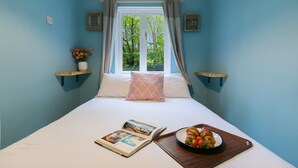 Um quarto com cama, janela com cortinas, mesa de cabeceira com um livro e um tabuleiro de comida, e uma prateleira com um vaso de flores.