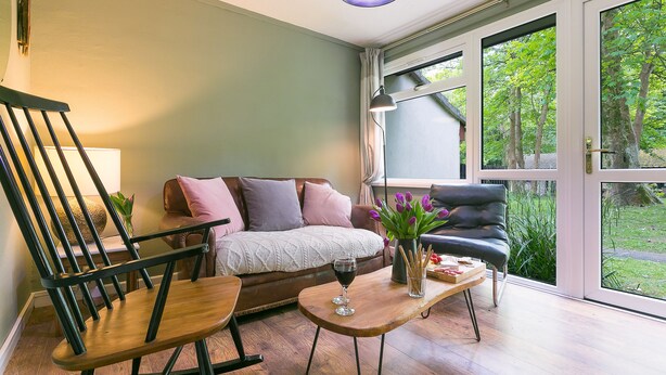 Uma sala de estar aconchegante com sofá, uma poltrona de balanço, mesa de centro e janela com vista para o verde.