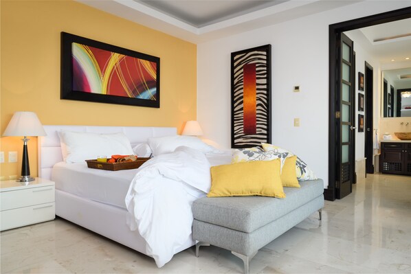 A modern bedroom with a bed, bedside tables, a sofa, and a large abstract painting on the wall.