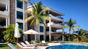 A pool area with lounge chairs and umbrellas, a clear blue pool, and a multi-story building with balconies. - Hacienda de Mita 506 by Tripwix (Punta de Mita)