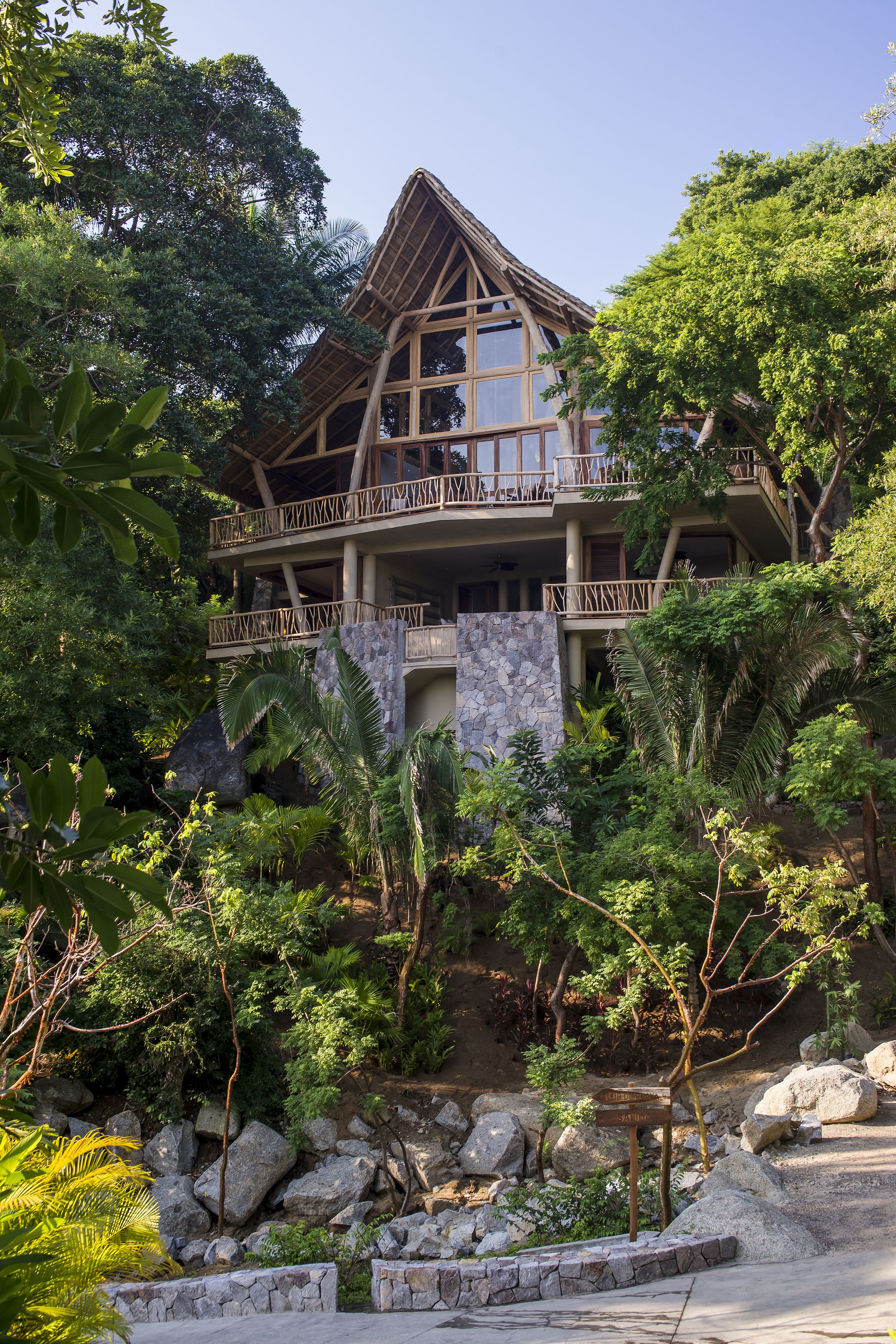 Un edificio de madera de dos pisos con balcones, rodeado de abundante vegetación y rocas.