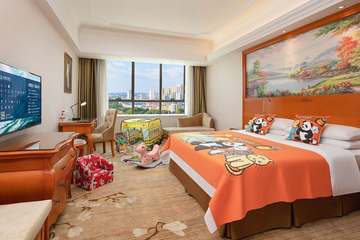 A hotel room with a large bed, a desk, a television, and a city view.
