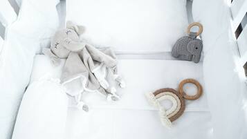 A white crib with a plush elephant toy, a knitted elephant keychain, and a macrame rattle.