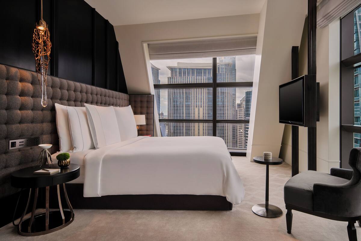 Habitación de hotel moderna con una cama grande, un televisor, una mesita auxiliar y vistas a la ciudad.