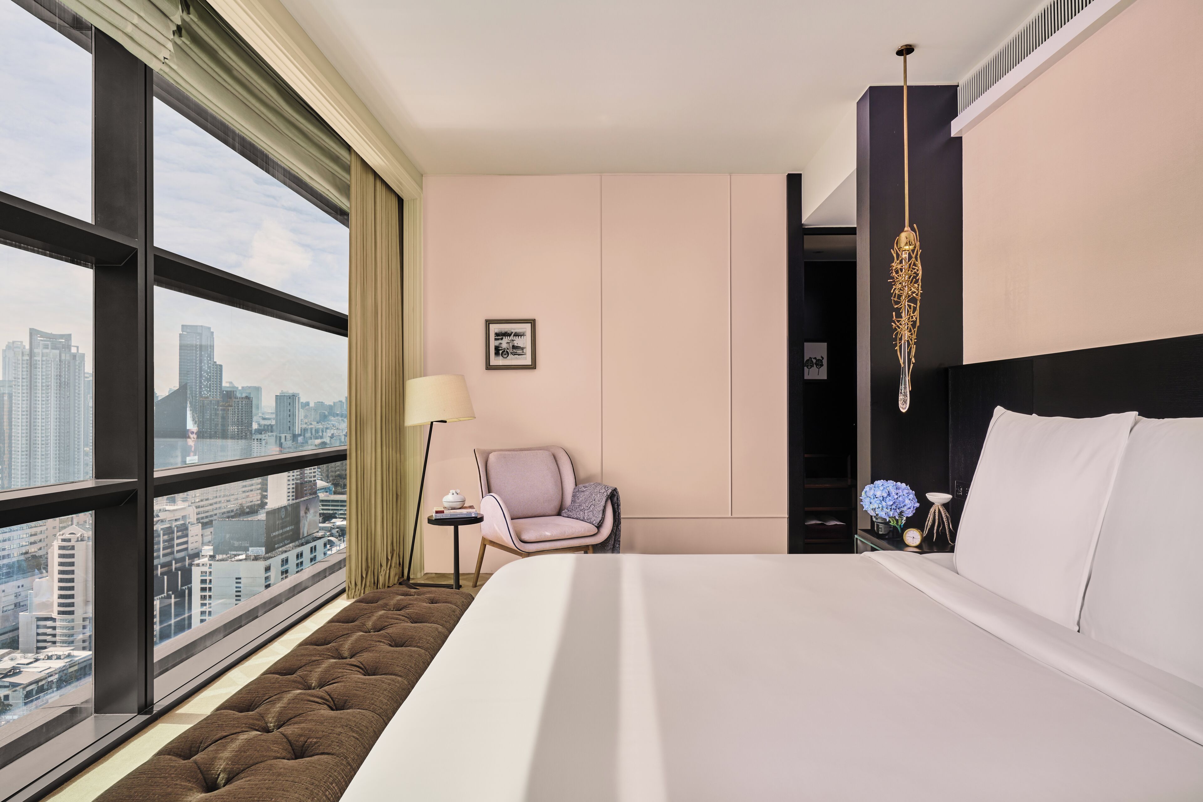 A hotel room with a large window, a bed, a chair, and a nightstand.