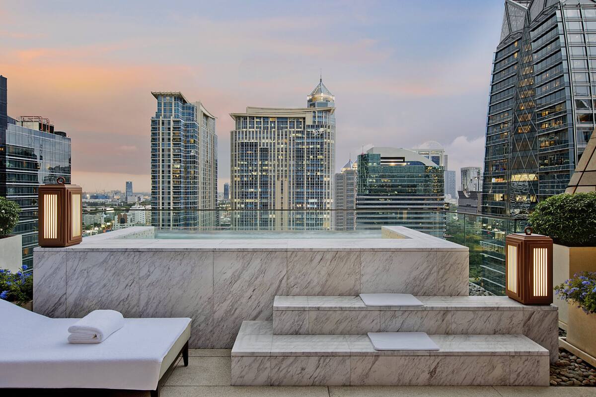 Terraza en la azotea con cama y zona de estar, con vistas al horizonte urbano.